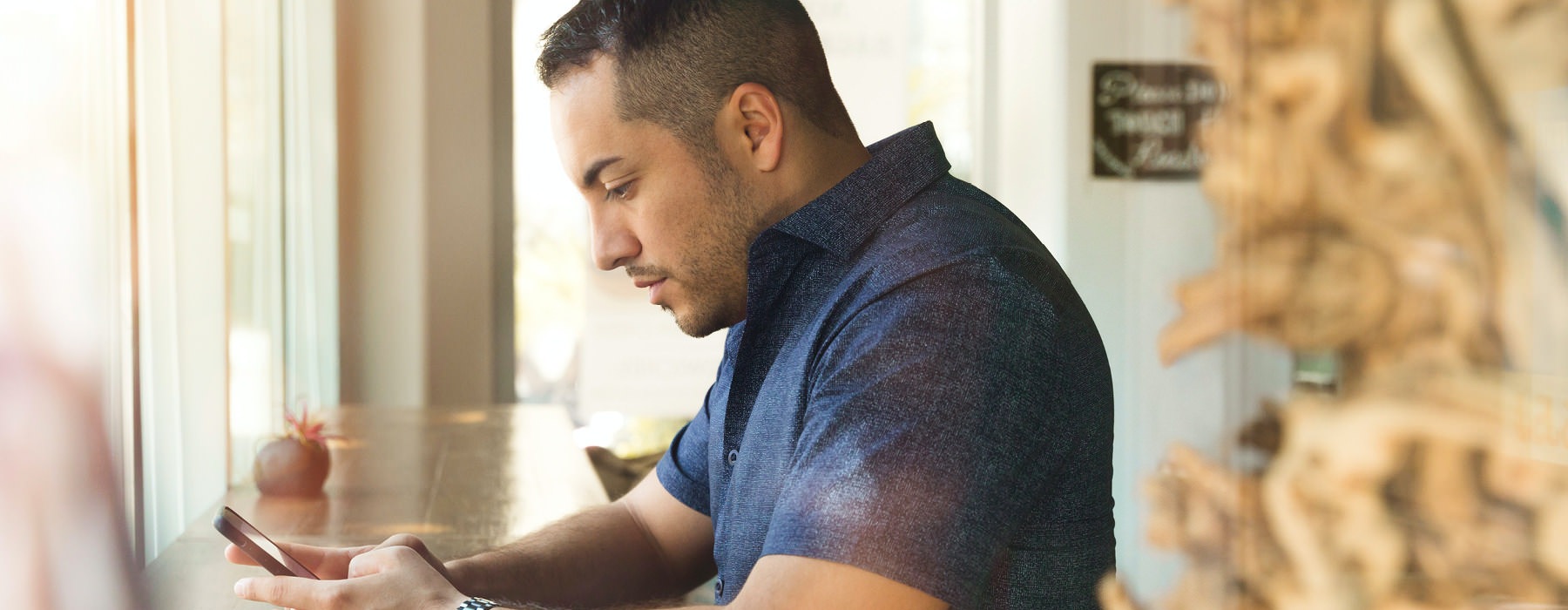 young man texts on his phone at window counter in neighborhood restaurant